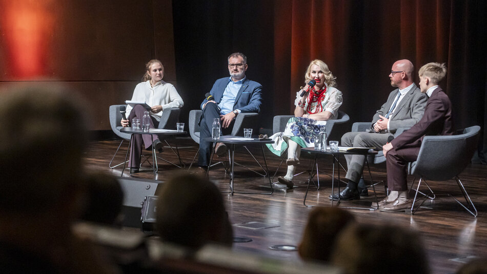 grupa ludzi siedzi na scenie otoczona widownią