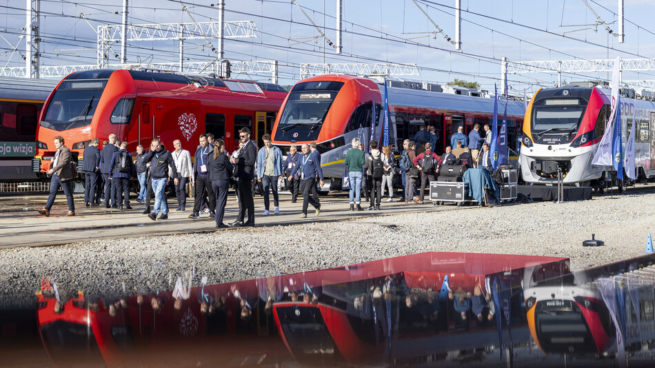 kilka pociągów stoi obok siebie, w okół nich chodzą ludzie