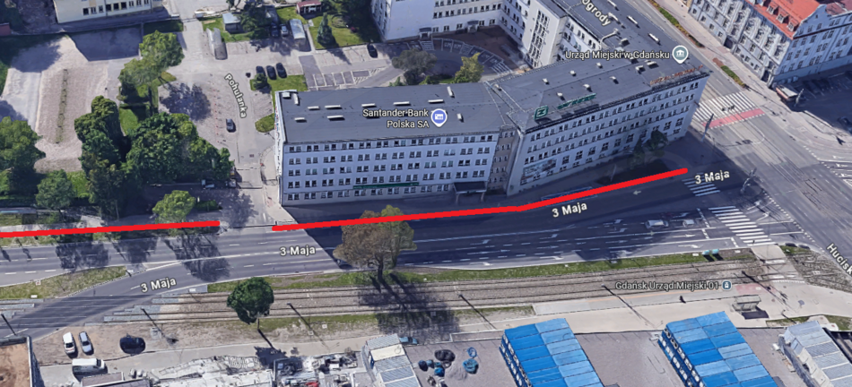 Na zdjęciu widać skrzyżowanie ulicy 3 Maja w Gdańsku, obok budynku Urzędu Miejskiego. Wzdłuż krawędzi ulicy biegnie czerwona linia, zaznaczająca fragment drogi rowerowej.