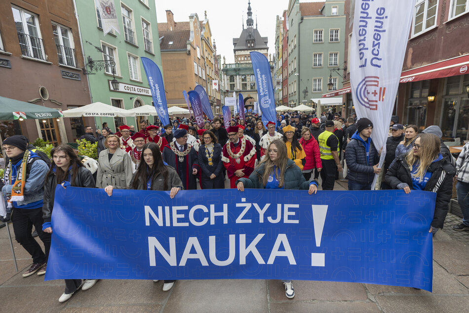 na zdjęciu barwna parada, na pierwszym planie młode dziewczęta niosą niebieski baner z białym napisem niech żyje nauka