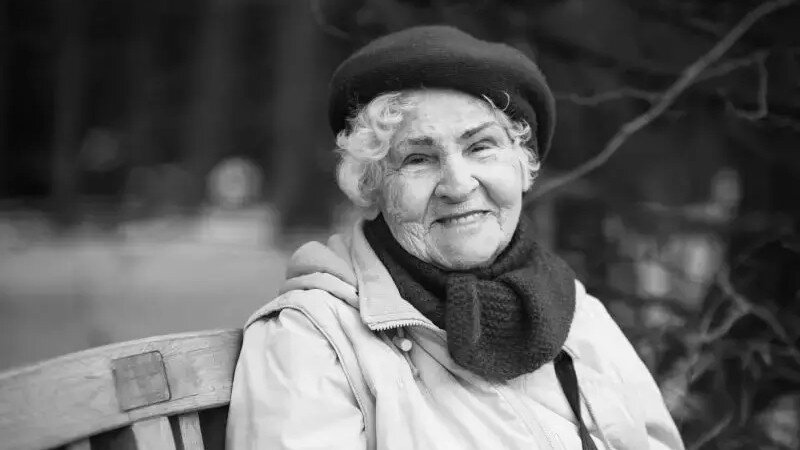 Czarno-białe zdjęcie. Uśmiechnięta starsza pani w berecie, szalu i kurtce