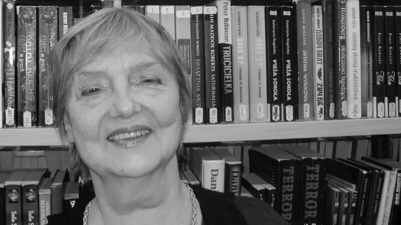 Czarno-białe zdjęcie. Uśmiechnięta twarz starszej kobiety na tle półek z książkami