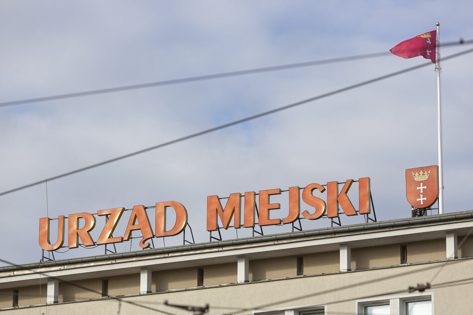 Na dachu budynku widoczny jest duży napis „Urząd Miejski” w pomarańczowym kolorze, obok którego znajduje się herb Gdańska. Nad konstrukcją powiewa czerwona flaga miasta z białym krzyżem i koroną. 
