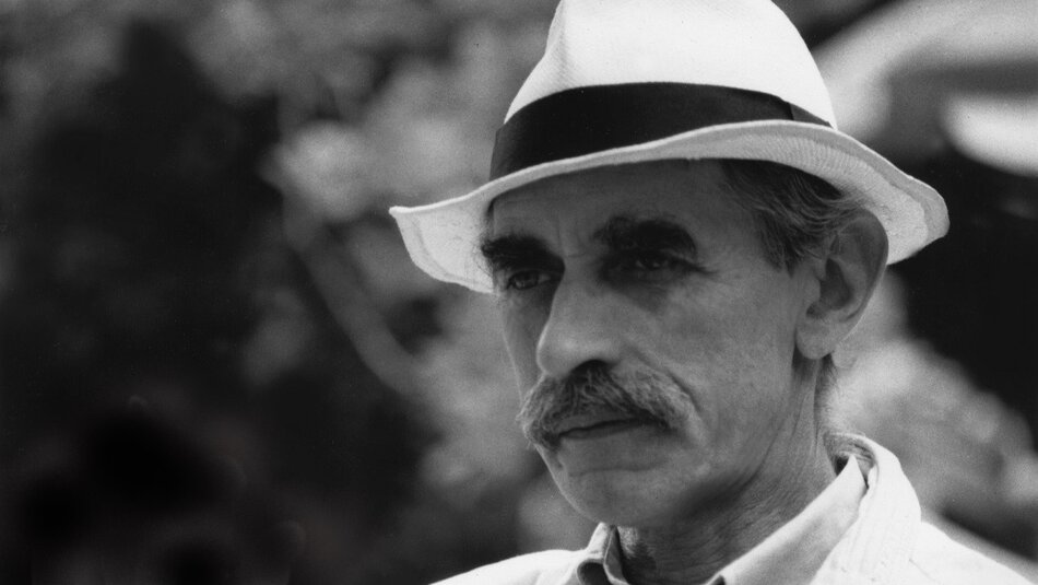 Mężczyzna o szczupłej twarzy, w jasnym kapeluszu, z wąsem.