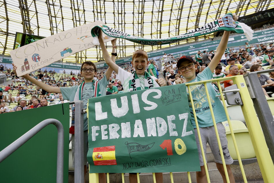 Młodzi kibice na trybunie meczowej trzymają tablicę z napisem Luis Fernandez i szalik z napisem Conrado 