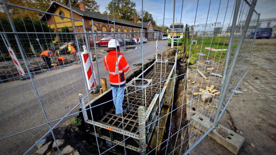 na zdjęciu kobieta w robotniczym stroju, obok niej fragmenty budowanych fundamentów