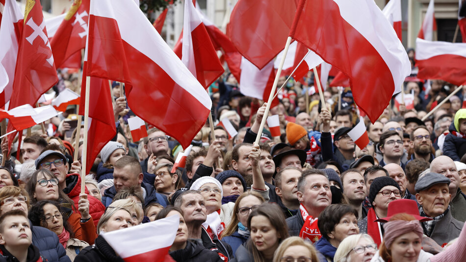 duże skupisko ludzi stojących obok siebie. Pomiędzy nimi dużo dwubarwnych flag