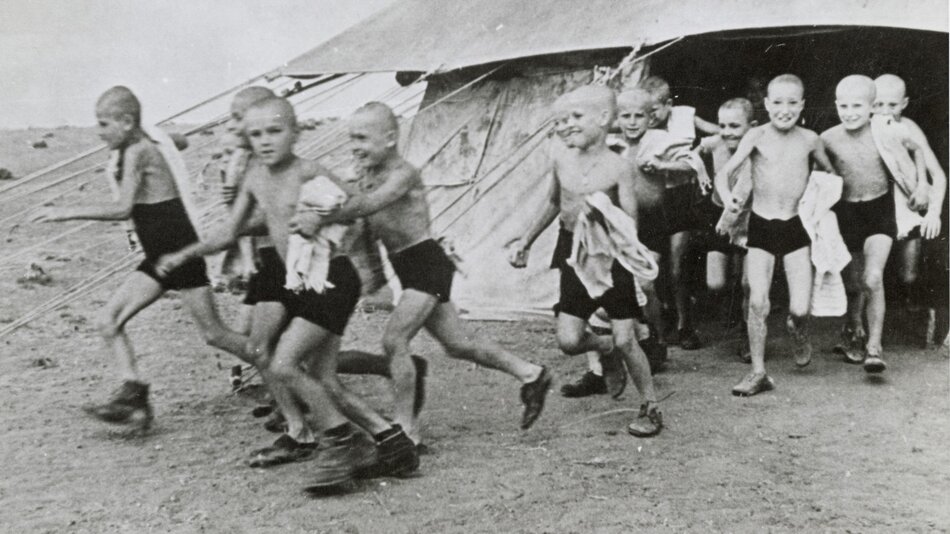 Grupa chłopców wybiegających z namiotu, są bez koszulek, zapewne panuje upał
