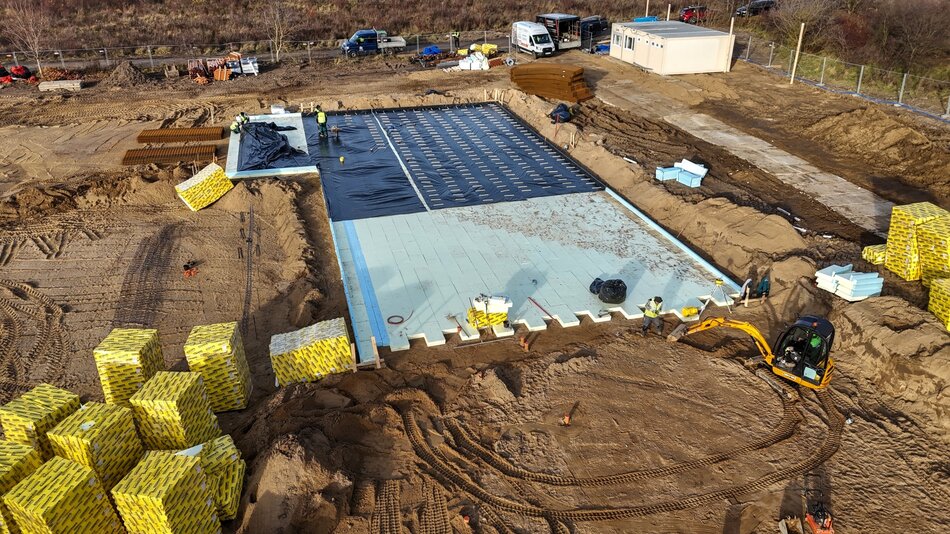 plac budowy widziany z drona, na gruncie ułożone są jasne płyty, widać kilku robotników