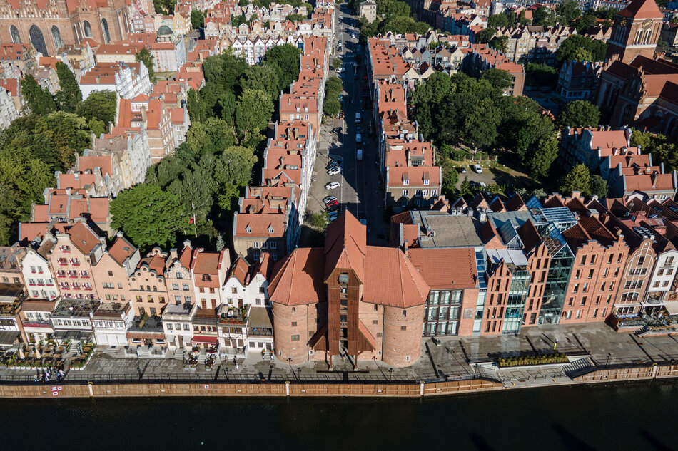 zdjęcie z drona, widać gęstą zabudowę starego miasta gdańska, to liczne kamienice, widać też zabytkowy budynek dawnego żurawia, w dole zdjęcia płynie rzeka