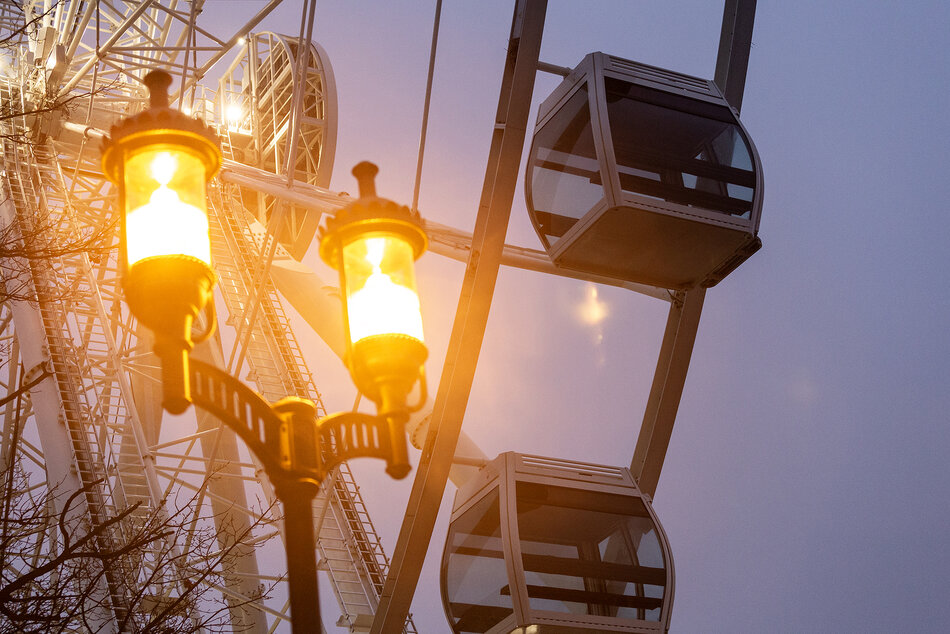 Fragment koła widokowego z widocznymi dwoma gondolami, na pierwszym planie latarnia miejska w starym stylu dająca ciepłe światło.