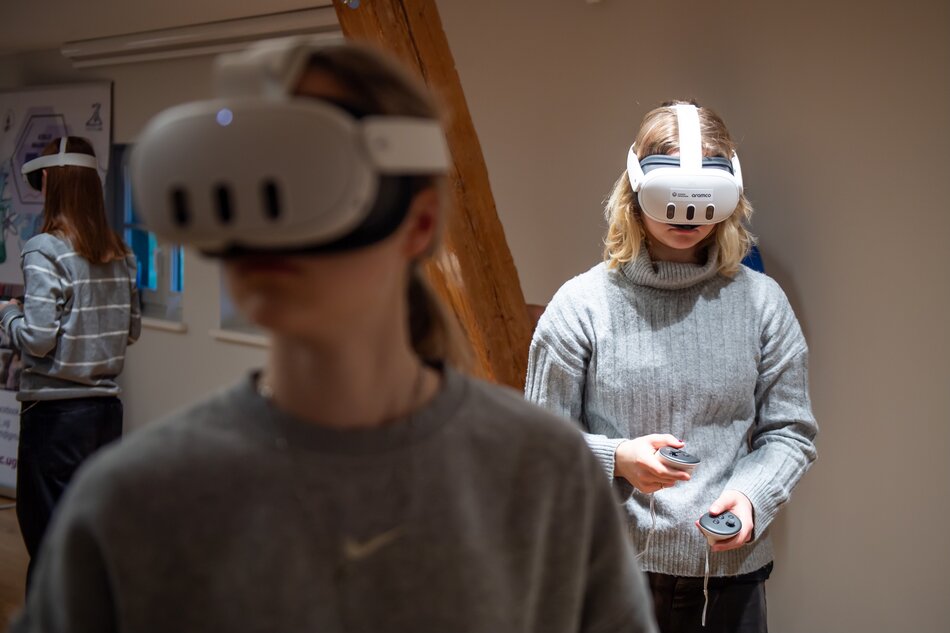 Troje młodych ludzi w goglach VR na twarzach stoi w sali.