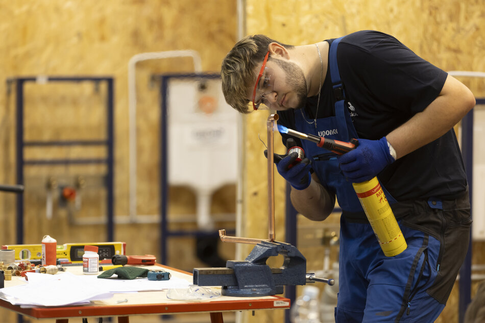 młody chłopak w okularach ochronnych pochyla się z lutownicą nad rurką miedzianą