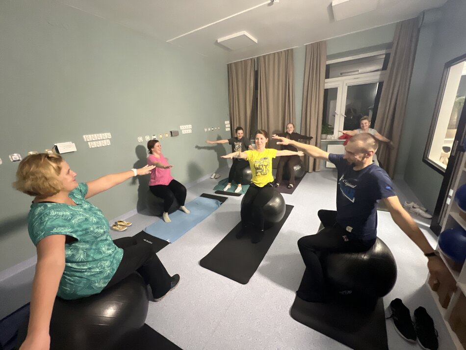 Osoby siedzą na piłkach i ćwiczą. 