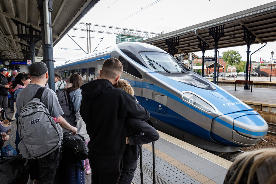 Pociąg Pendolino podjeżdża na peron, na którym stoją podróżni z walizkami.