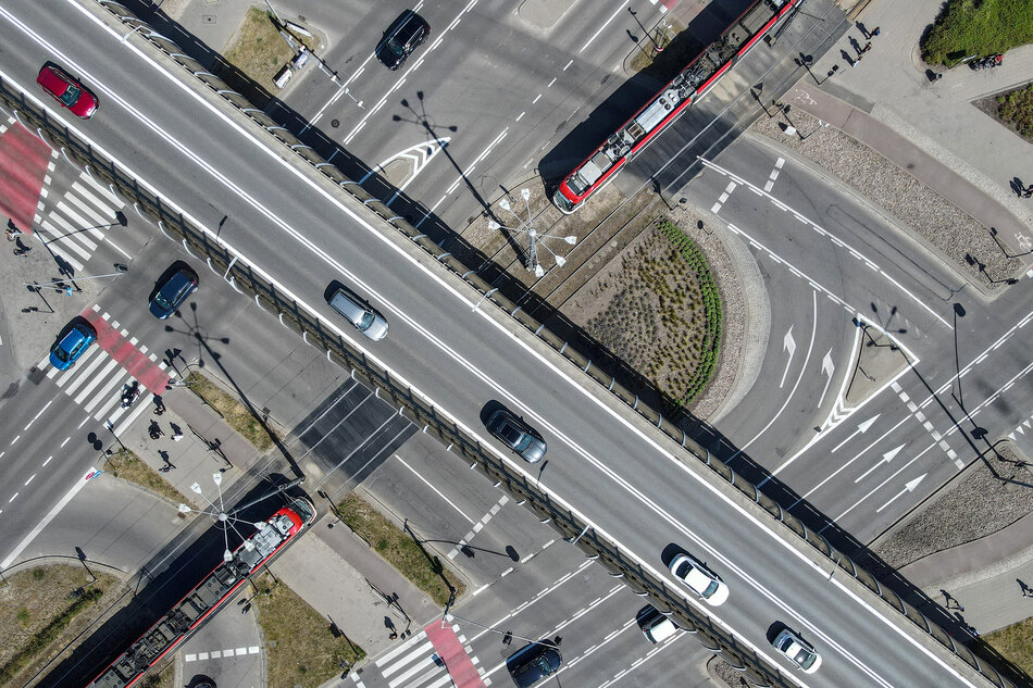 Zdjęcie z lotu ptaka ukazuje wielopoziomowe skrzyżowanie z estakadą, po której poruszają się samochody w obu kierunkach. Pod estakadą widoczny jest ruch tramwajów, pieszych i pojazdów, tworzących złożony układ komunikacyjny tego fragmentu miasta. 