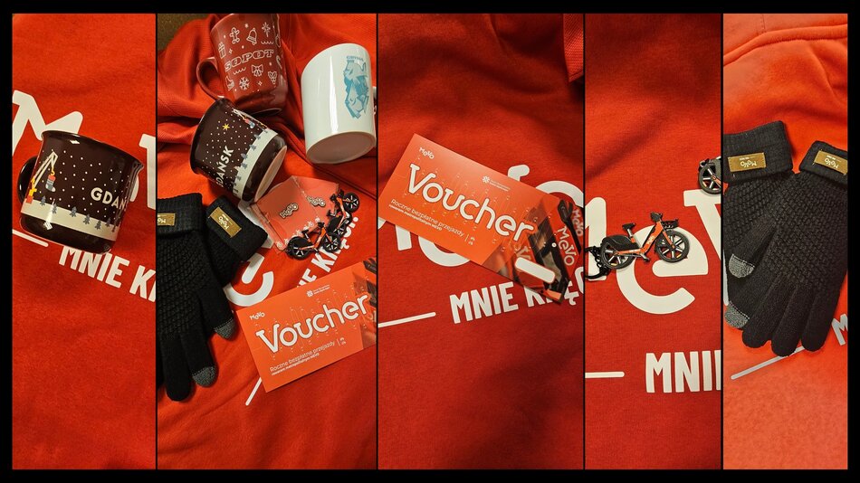 Zdjęcie przedstawia zestaw upominków, w tym kubki z miejskimi motywami, rękawiczki, miniaturowy rower Mevo oraz voucher na roczne przejazdy. Wszystkie gadżety ułożono na czerwonej koszulce z nadrukiem, tworząc spójną kompozycję prezentową. 