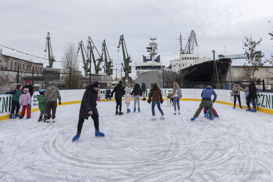 kilka osób jeździ na łyżwach po lodowisku - wokół stoczniowe widoki 