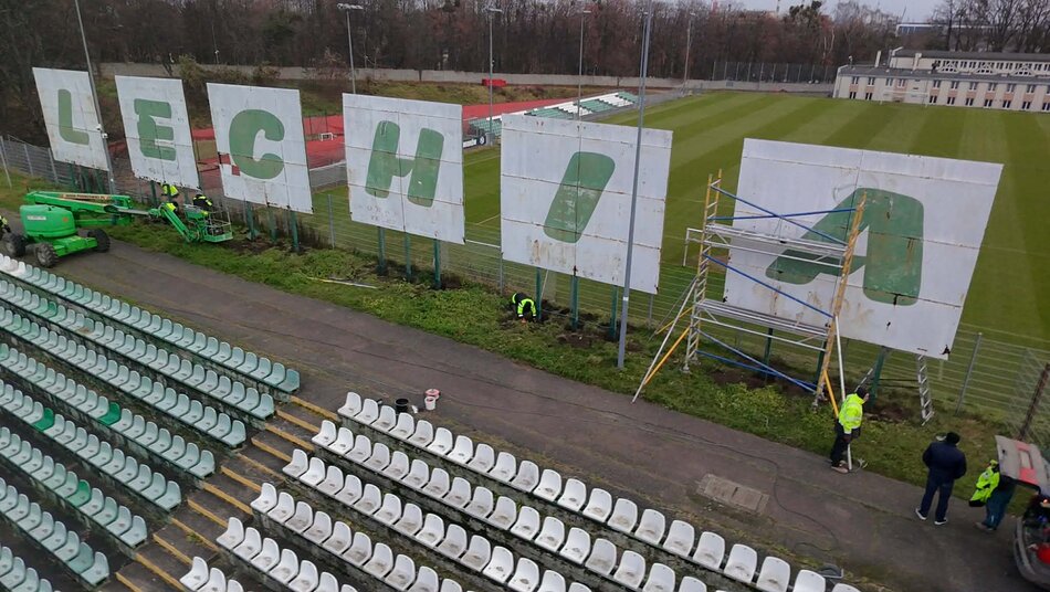 Wielki napis LECHIA na blaszanych tablicach ustawionych na stadionie piłkarskim. Przy napisie stoi rusztowanie, pracują ludzie.