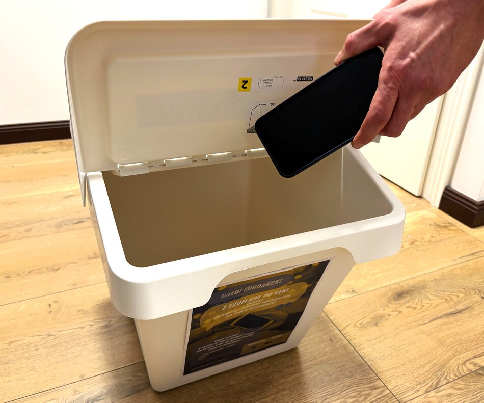 Ręka trzymająca telefon nad plastikowym pojemnikiem z napisem „Z szuflady do ręki”.
