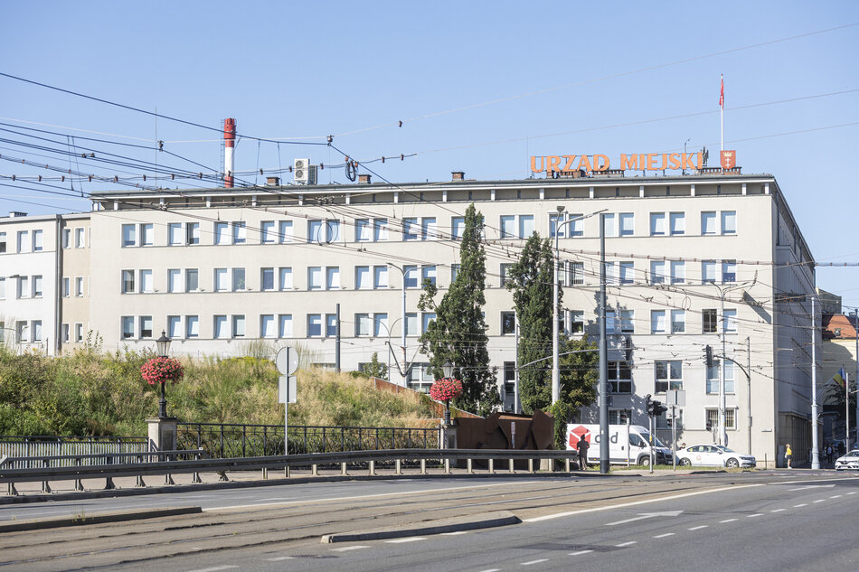 duży szary budynek z czerwono-pomarańczowym znakiem z napisem Urząd Miejski na górze