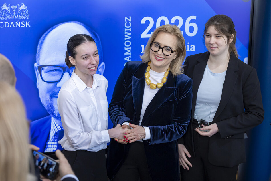 Kobieta składa gratulacje uczennicy, obok stoi druga uczennica, wszystkie się uśmiechają. 