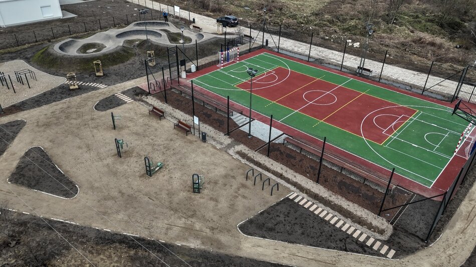 zdjęcie z drona, widać na nim bordowe boisko do gry, w tle betonowy szary pamptrak