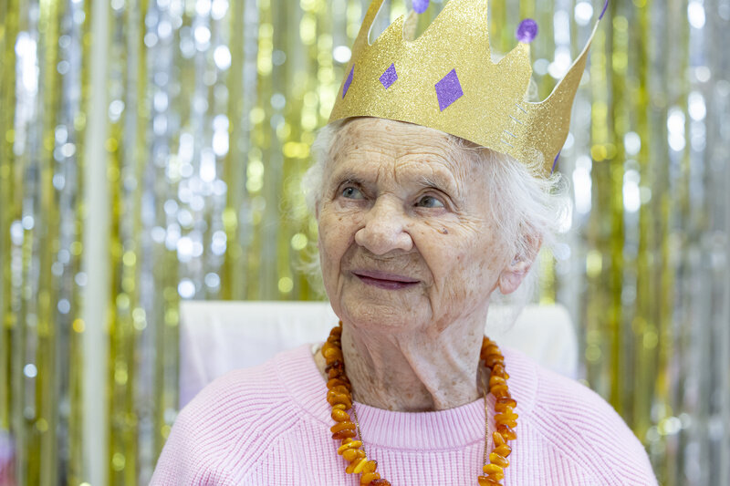 na zdjęciu starsza kobieta z białymi włosami, z papierową koroną na głowie