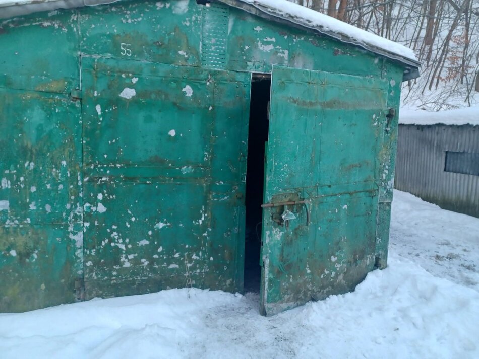 Stary, zielony garaż otoczony śniegiem. Drzwi do niego są uchylone
