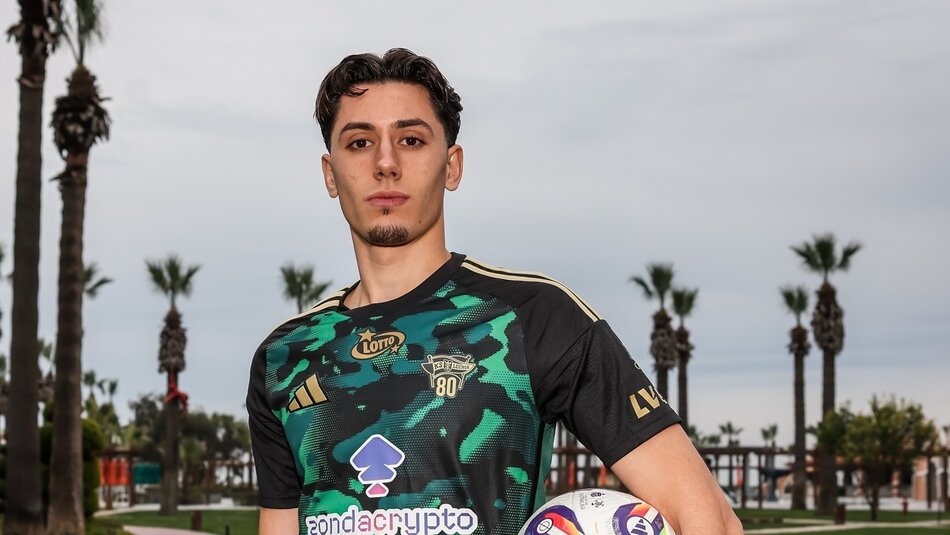 piłkarz na sesji zdjęciowej w zielono-czarnej koszulce. W tle palmy