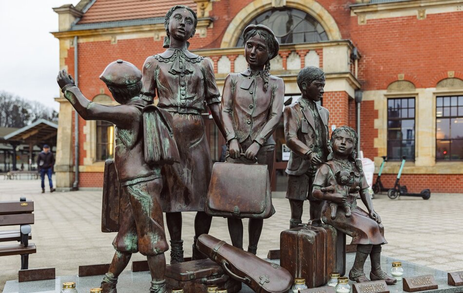 Brązowa rzeźba przedstawia grupę dzieci z walizkami, ukazanych w chwili rozstania i oczekiwania, z wyraźnie zaznaczonymi emocjami w postawach i gestach postaci. Pomnik stoi na placu przed ceglaną elewacją budynku i nawiązuje do historycznych losów dzieci zmuszonych do opuszczenia swoich domów. 