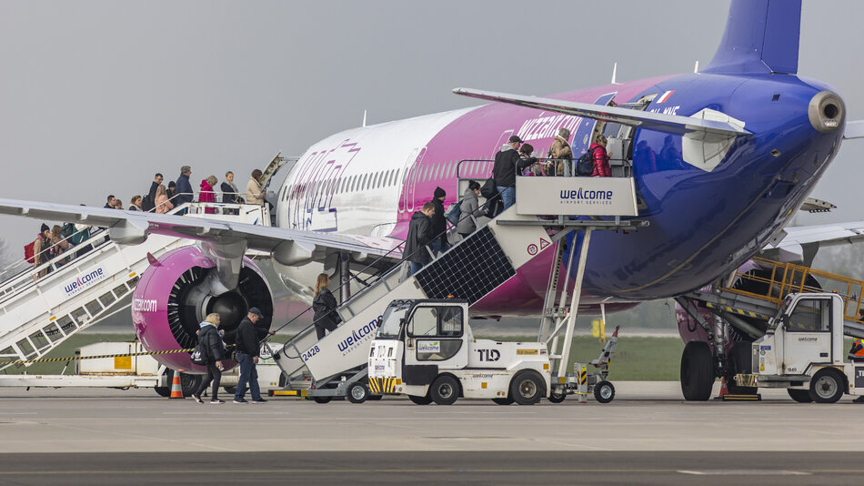  Duży odrzutowiec pasażerski zaparkowany na asfalcie na lotnisku. Odrzutowiec jest pomalowany w połączeniu różowych i niebieskich kolorów, a słowo Witamy napisane na biało na boku to trawione pole i pochmurne niebo.