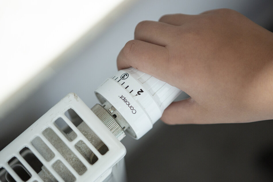 kaloryfer na głównym planie i ręka, która reguluje pokrętło