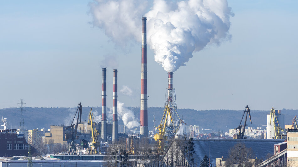 zakład przemysłowy z czterema wysokimi kominami, z jednego z nich wydostaje się gęsty słup pary
