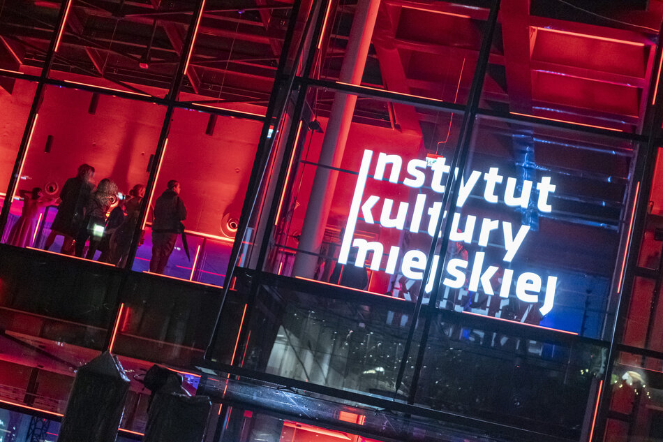Fragment budynku, w którym przez przeszkloną fasadę widać w środku ludzi. Obiekt jest podświetlony na czerwono. W witrynie okna napis Instytut Kultury Miejskiej.