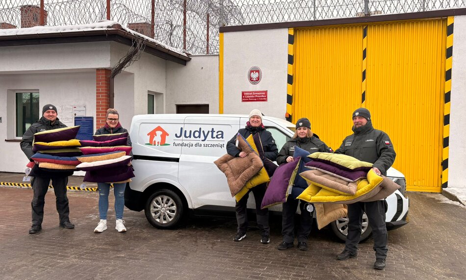 Pięć uśmiechniętych osób stoi przed samochodem dostawczym. W rękach mają legowiska dla psów