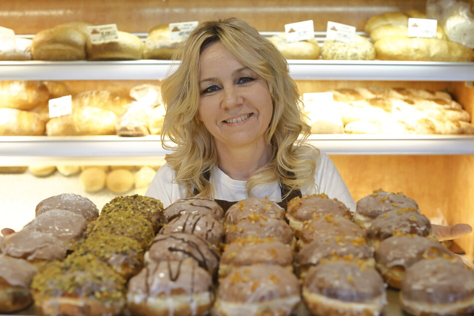 Kobieta uśmiechnięta - prezentuje blachę na której rzędami położone są pączki