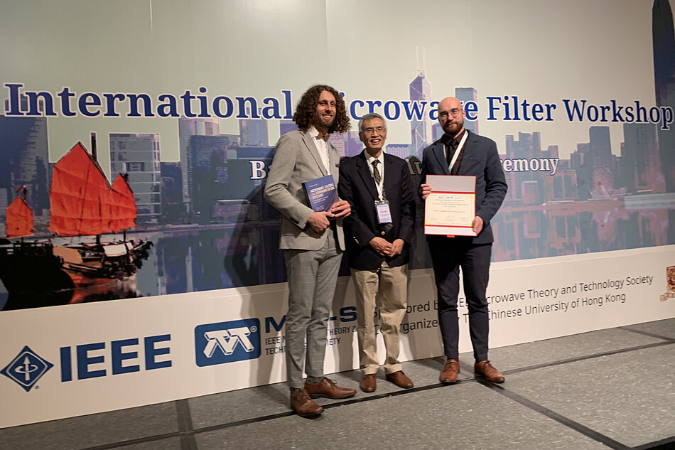 Trzech mężczyzn pozuje do zdjęcia na tle ścianki z napisami.