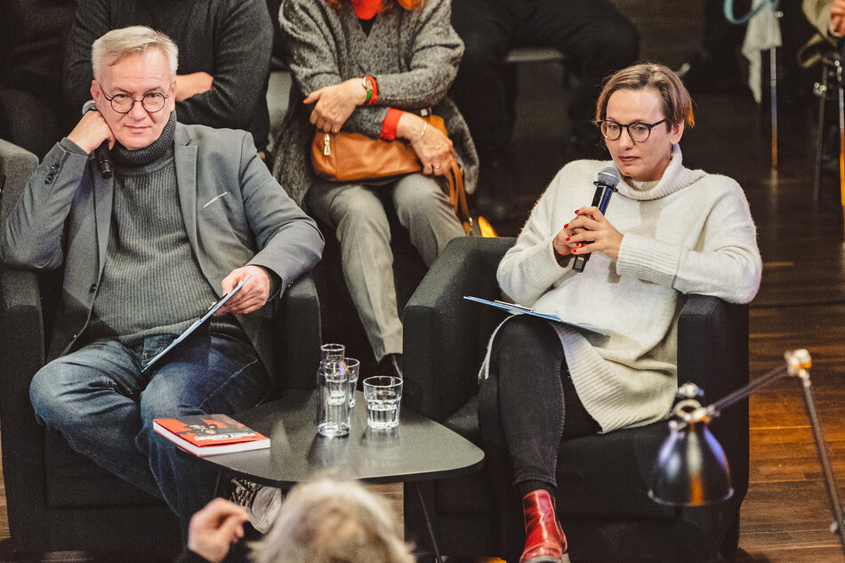 mężczyzna i kobieta siedzą przy stoliku. Mają mikrofon w ręce i rozmawiają