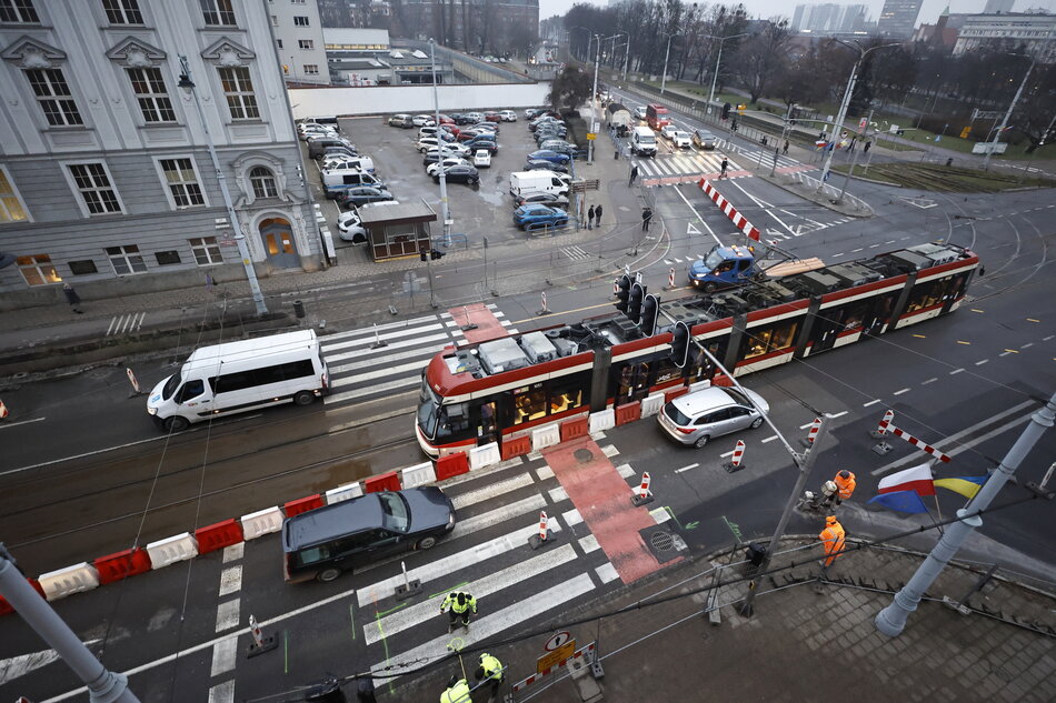 Widok skrzyżowania z wysokiego piętra okna budynku - widać jadący tramwaj i samochody