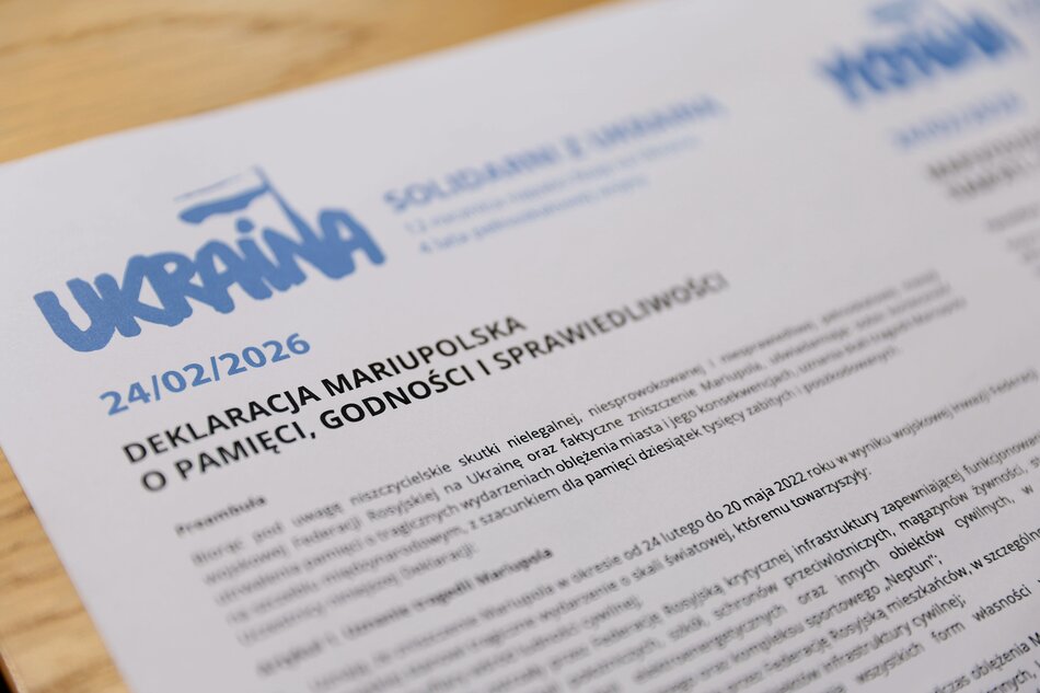 Na zdjęciu widać dokument zatytułowany „Deklaracja Mariupolska o Pamięci, Godności i Sprawiedliwości” z datą 24 lutego 2026 roku, upamiętniającą czwartą rocznicę inwazji na Ukrainę. Tekst preambuły odnosi się do tragicznego oblężenia Mariupola, niszczenia infrastruktury cywilnej oraz konieczności zachowania pamięci o dziesiątkach tysięcy ofiar