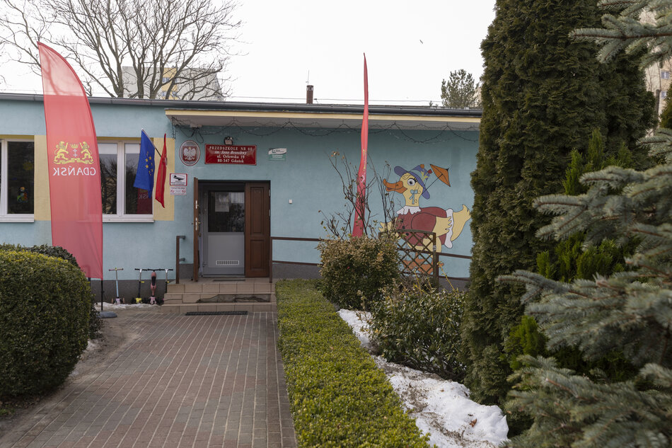 Na zdjęciu widać budynek. Przed wejściem do błękitnego obiektu rozciąga się chodnik z kostki brukowej, a elewację zdobi kolorowy malunek kaczora w kapeluszu. 