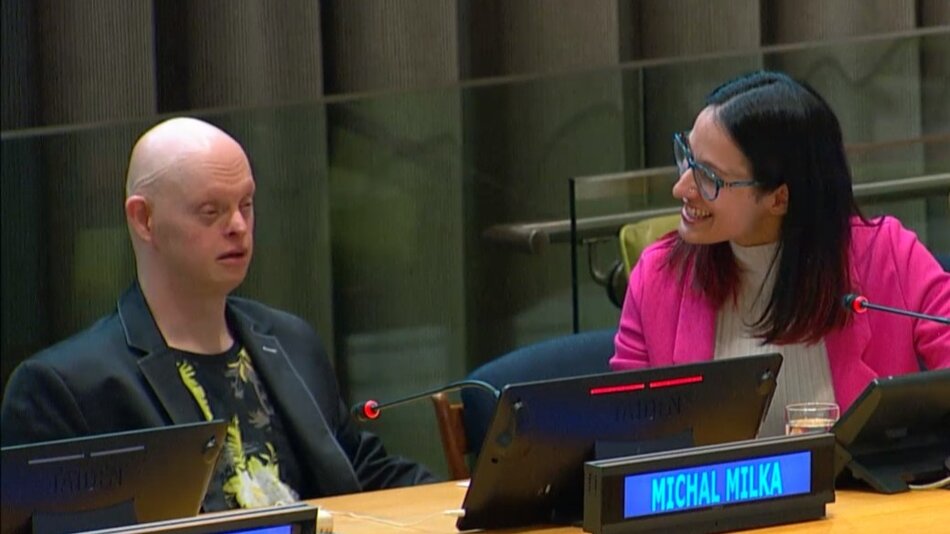 Po lewej stronie siedzi łysy mężczyzna, po prawej kobieta, która uśmiecha się do niego. Oboje siedzą w sali, mówią do mikrofonu