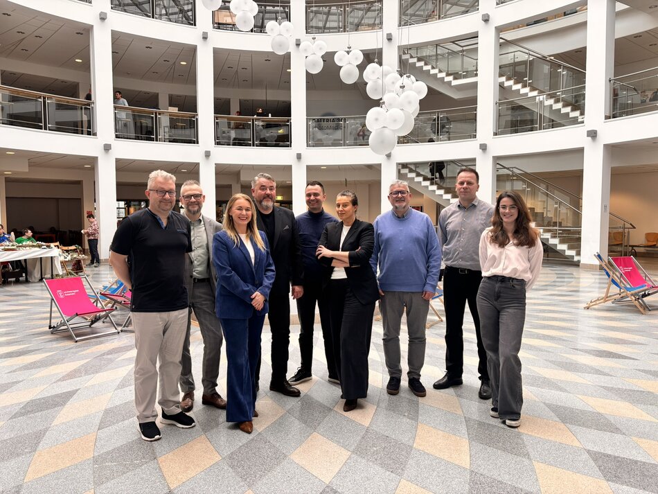 Grupa 9 ludzi stoi wewnątrz budynku i patrzy w obiektyw