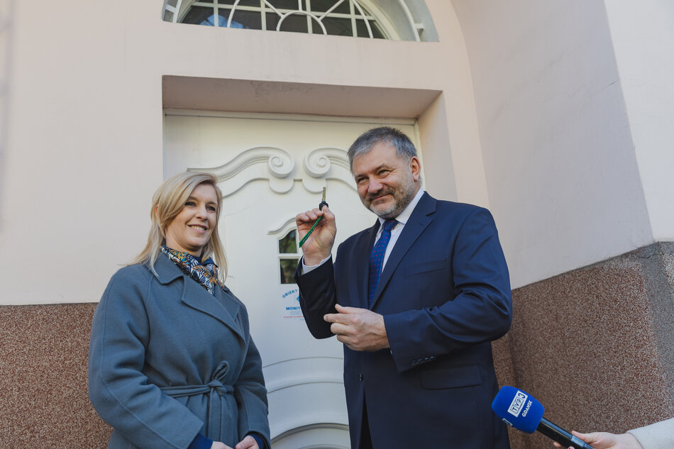 Kobieta i mężczyzna przed drzwiami starego budynku. Mężczyzna pokazuje klucz do drzwi.