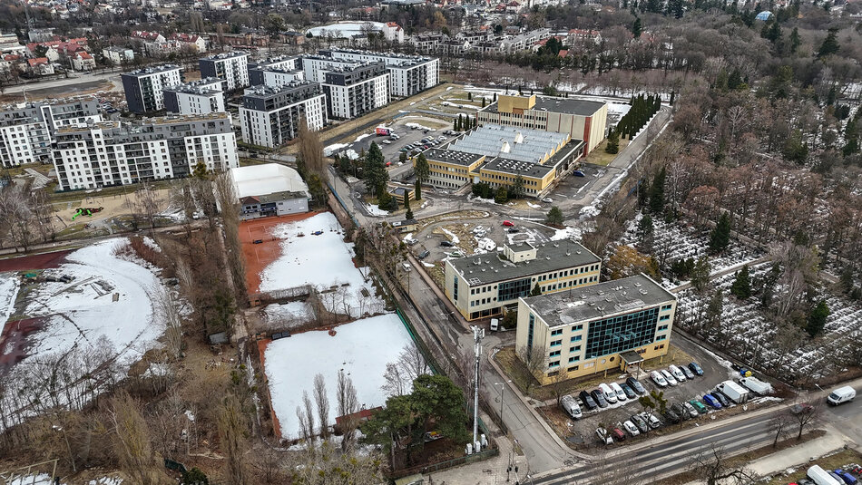 Zdjęcie z lotu ptaka, widok na część miasta. Widać bloki mieszkalne, biurowce, boiska przykryte warstwą śniegu i cmentarz.