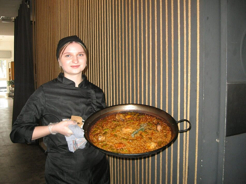 młoda kobieta w stroju kucharza pozuje z wielką patelnią wypełnioną jedzeniem
