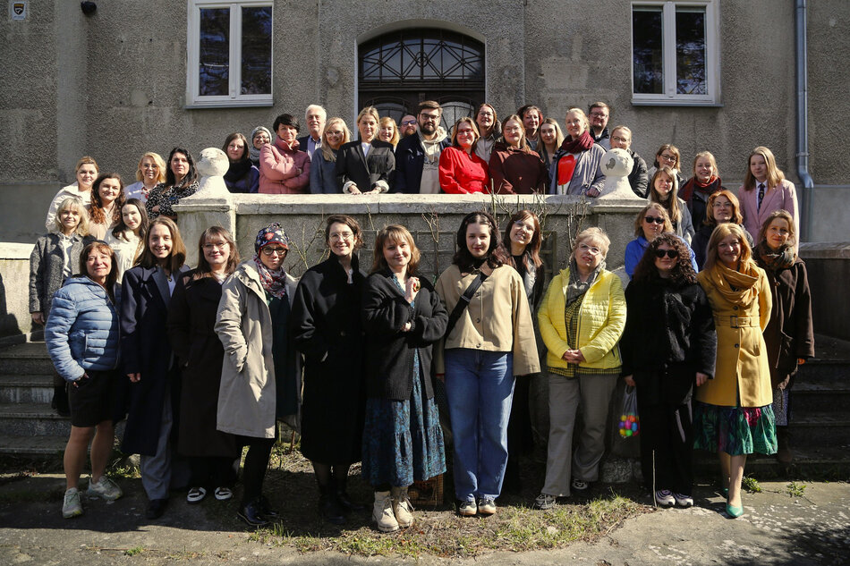 Około 40 osób stoi przed budynkiem, część z nich na schodach przed wejściem, i pozuje do zbiorowej fotografii.