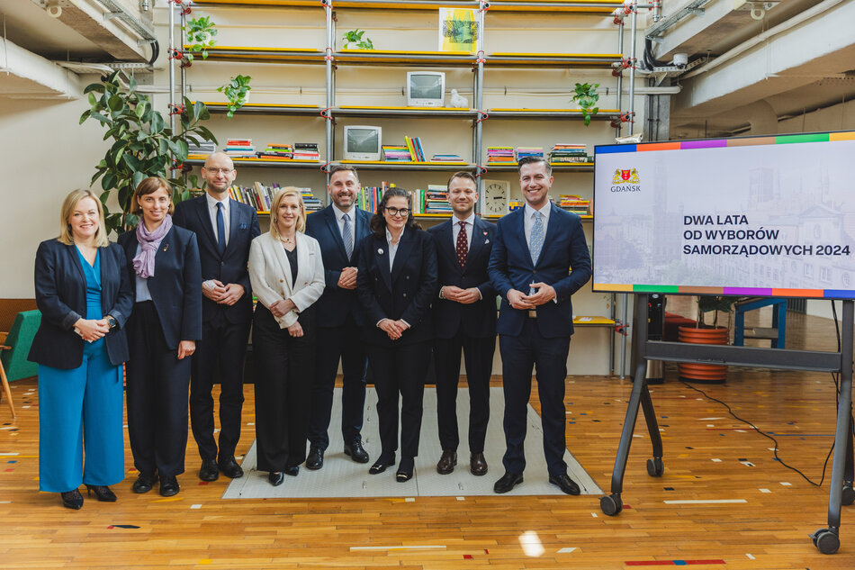 Na zdjęciu stoi w rzędzie kilka osób w oficjalnych strojach (od lewej): radna Katarzyna Czerniewska, wiceprezydent Monika Chabior, dyrektor Piotr Kryszewski, wiceprezydent Emilia Lodzińska, wiceprezydent Piotr Borawski, prezydent Aleksandra Dulkiewicz, radni Mateusz Skarbek oraz Cezary Śpiewak-Dowbór