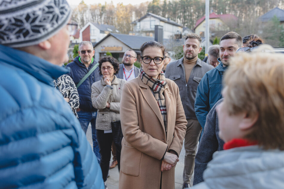 na zdjęciu prezydent gdańska w karmelowym płaszczu otoczona wokół grupą dorosłych osób